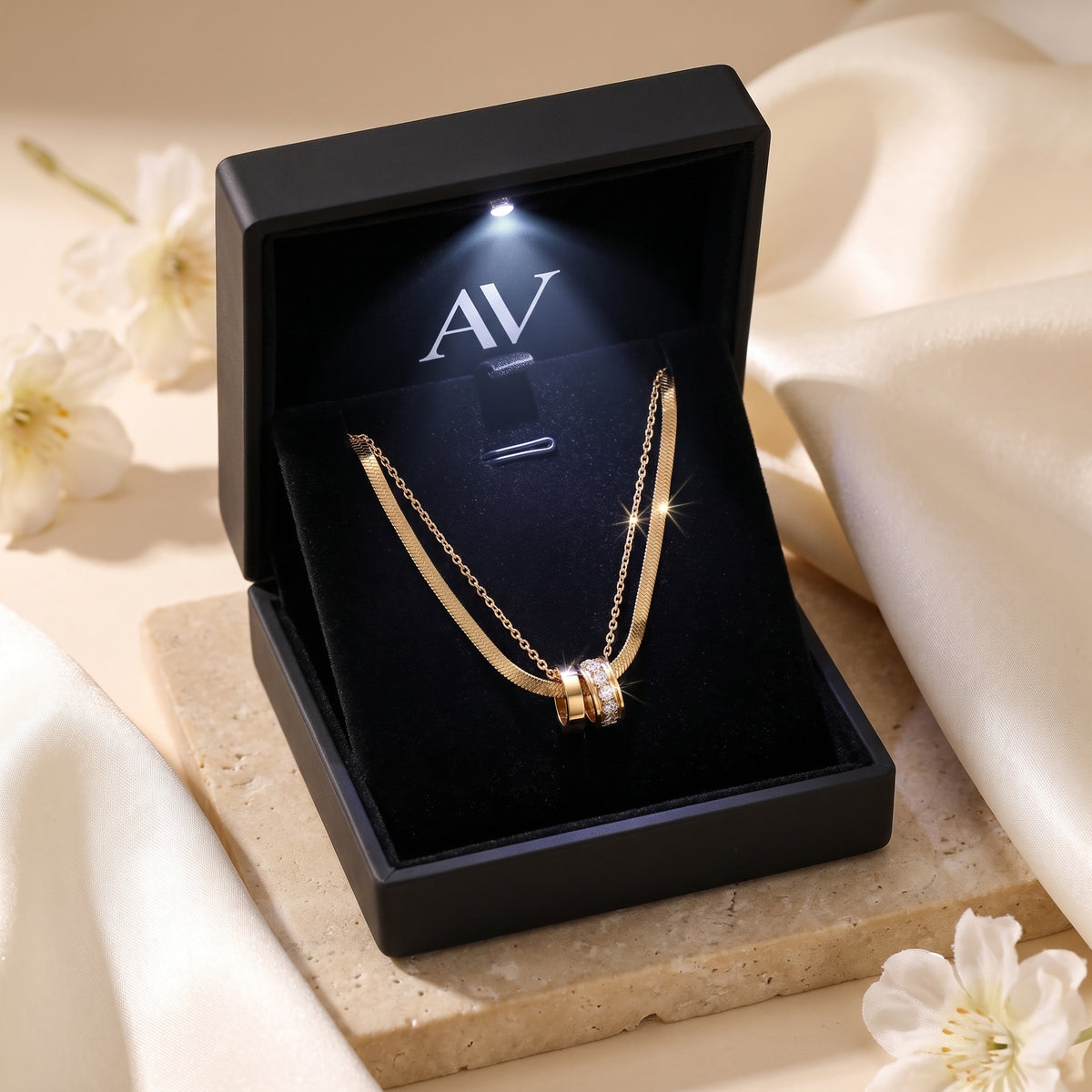 Gold layered necklace inside a black LED-lit presentation box with AV branding.