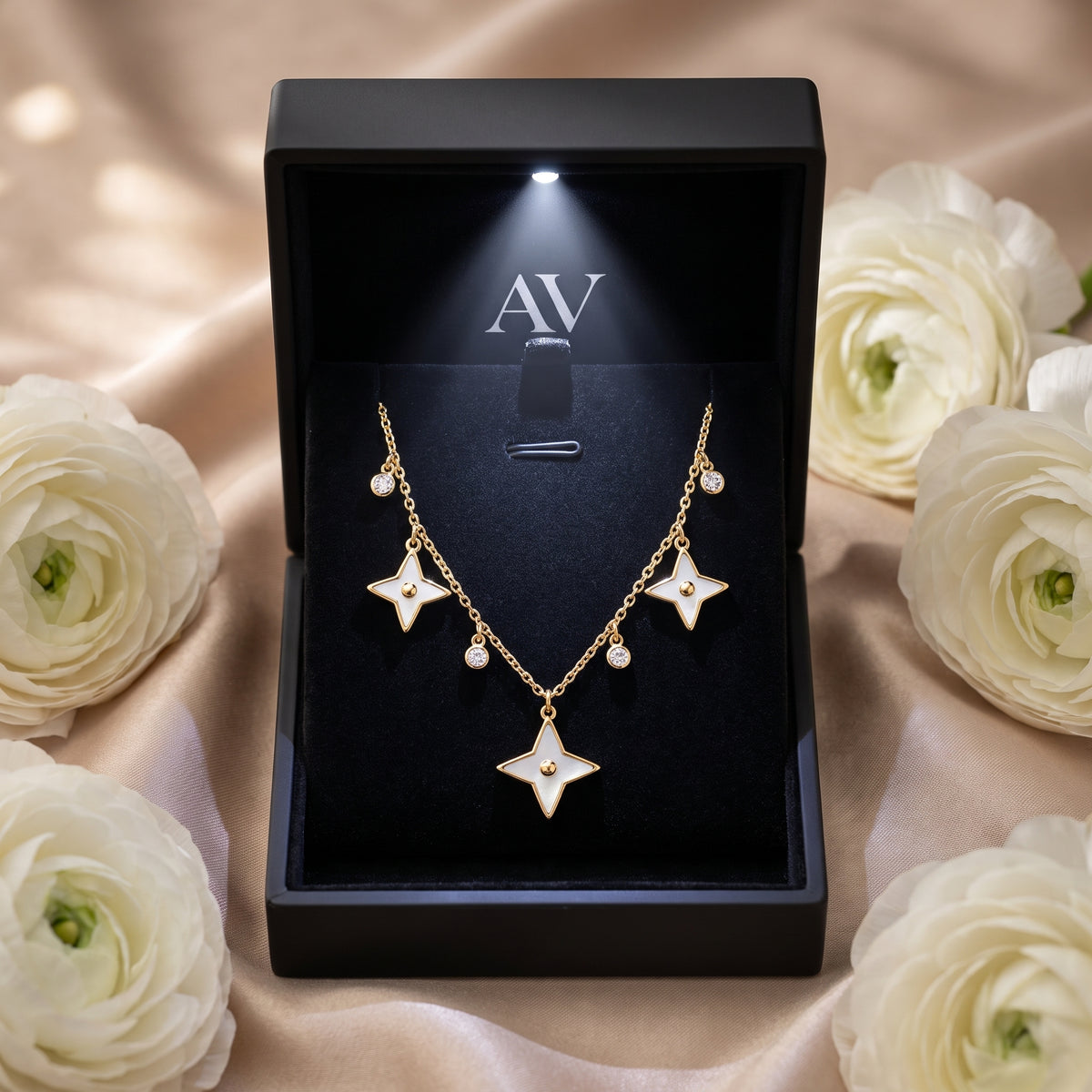 Gold star pendant necklace displayed in a lighted black gift box surrounded by white flowers.