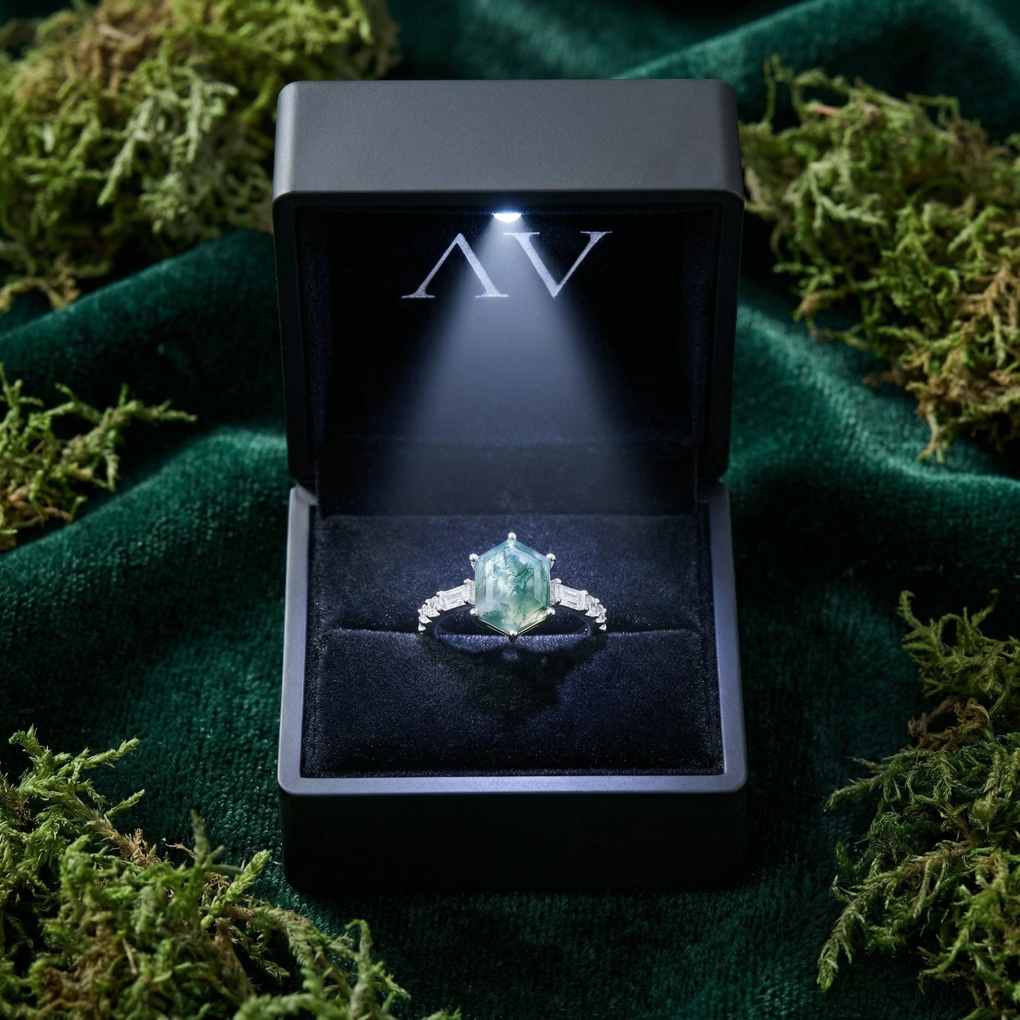 Hexagonal moss agate sterling silver ring in a lighted black gift box on green velvet and moss.