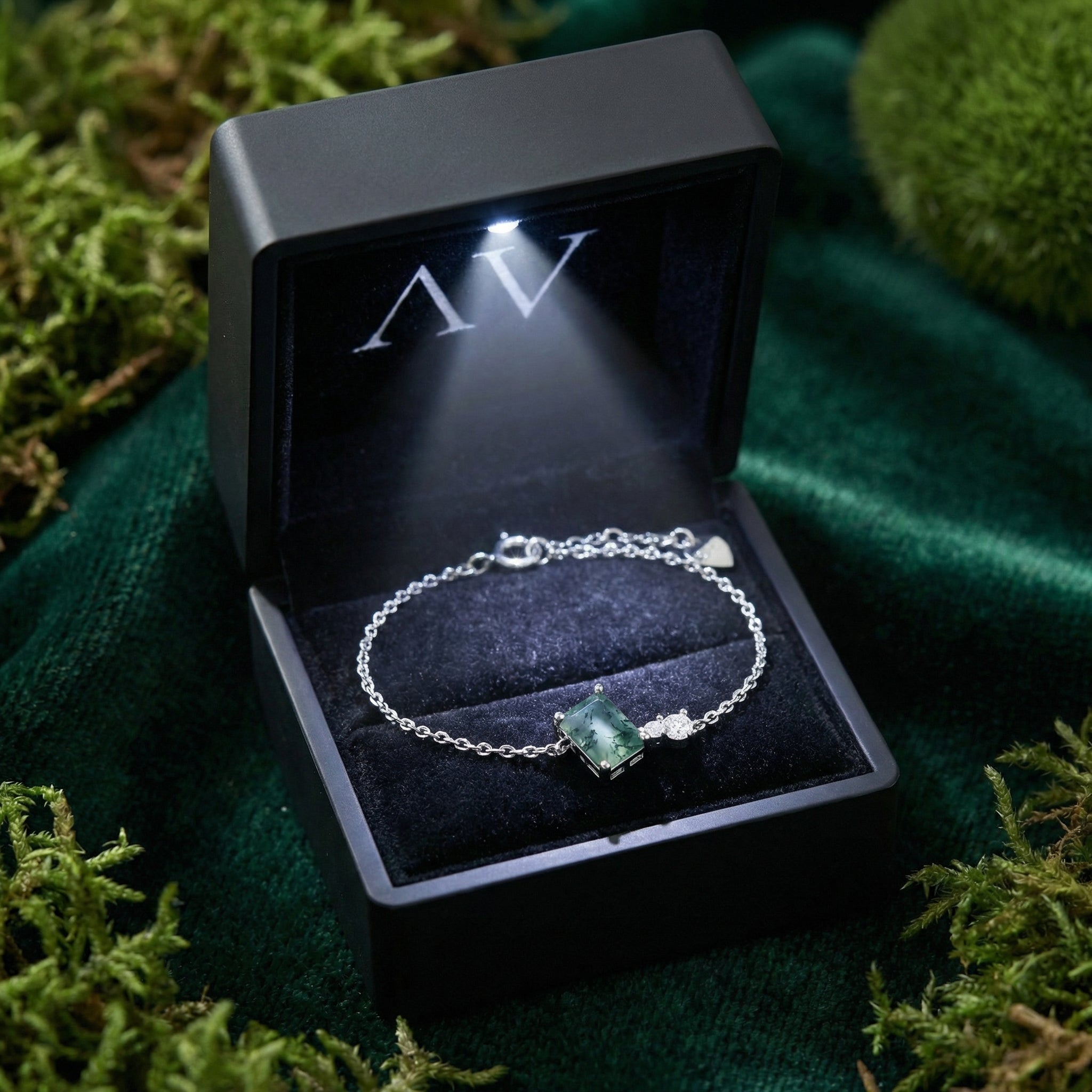 Natural moss agate sterling silver bracelet presented in a black light-up gift box on a mossy green background.