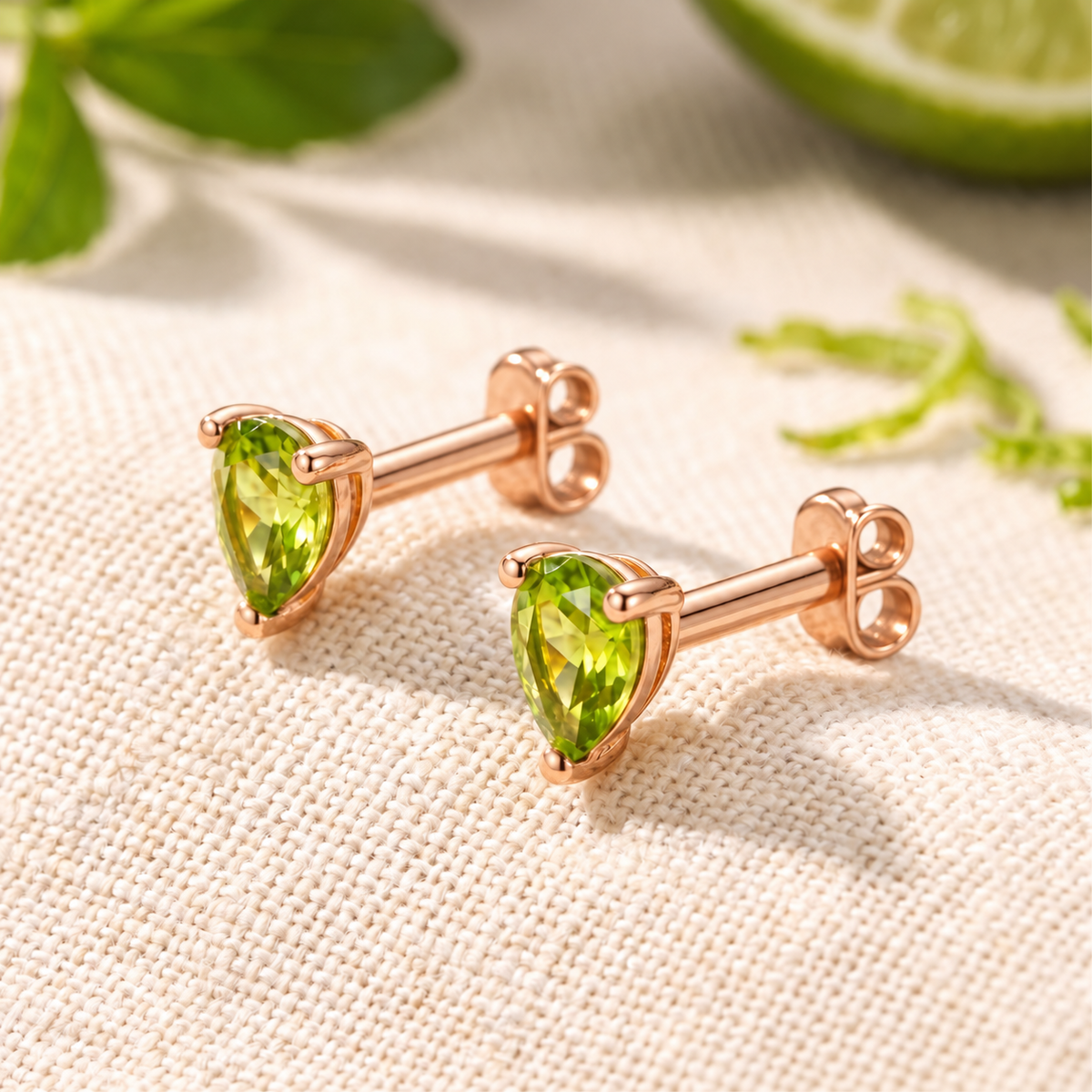 Pair of pear-cut green simulated peridot stud earrings in rose gold with butterfly backs on textured fabric.