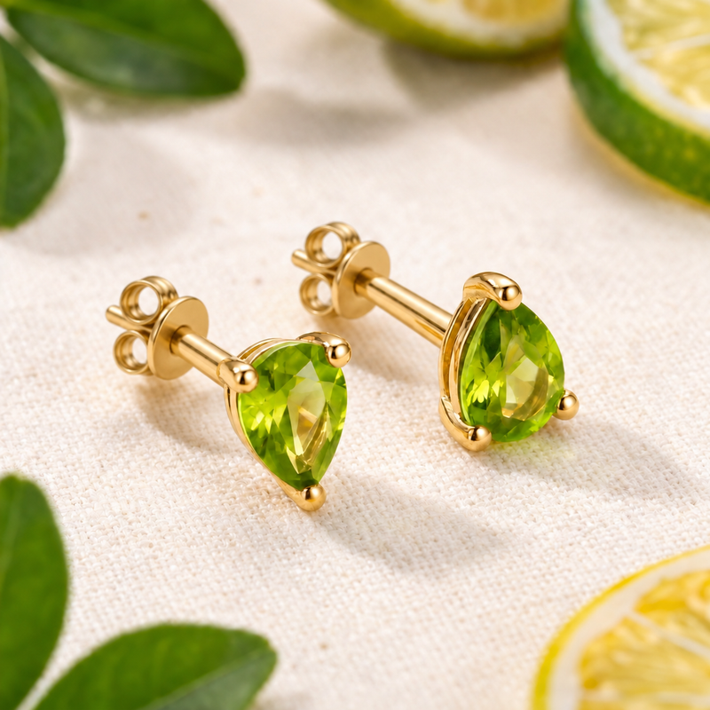 Pair of pear-cut green simulated peridot stud earrings in yellow gold with butterfly backs beside lime slices.