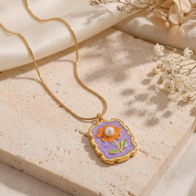 Flat-lay Amorina necklace on textured stone, showing a purple floral pendant with orange flower and simulated pearl.