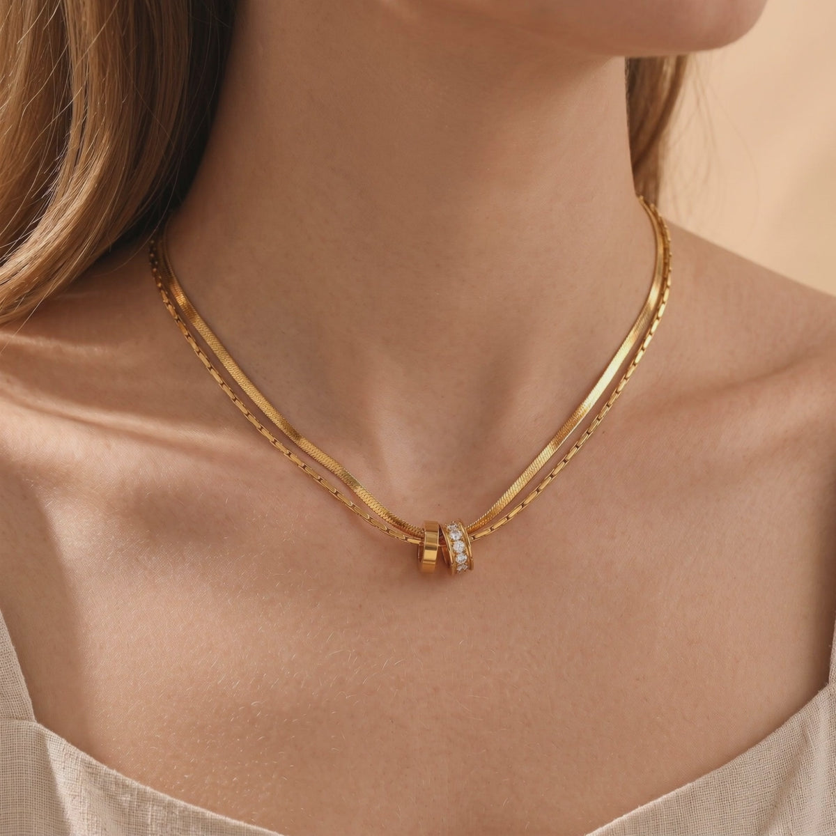 Double-layered gold-finish necklace with plain and cubic zirconia ring pendants worn at the neck.