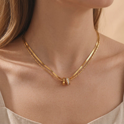 Double-layered gold-finish necklace with plain and cubic zirconia ring pendants worn at the neck.