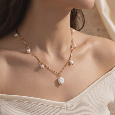 Gold-tone necklace with irregular white pearls worn around a model's neck, with the largest pearl at center.