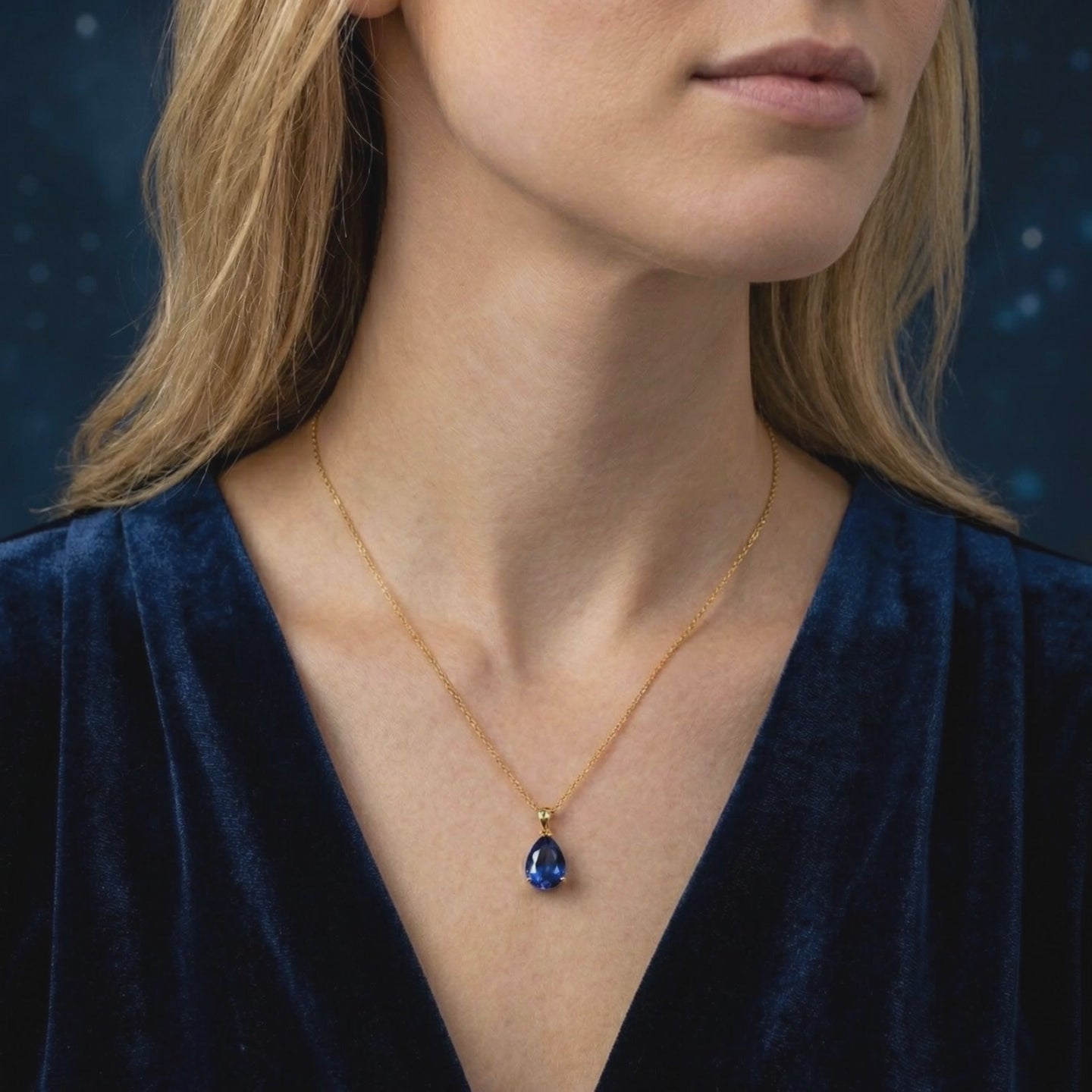 Model wearing a simulated sapphire pendant necklace in solid gold over a navy V-neck top.