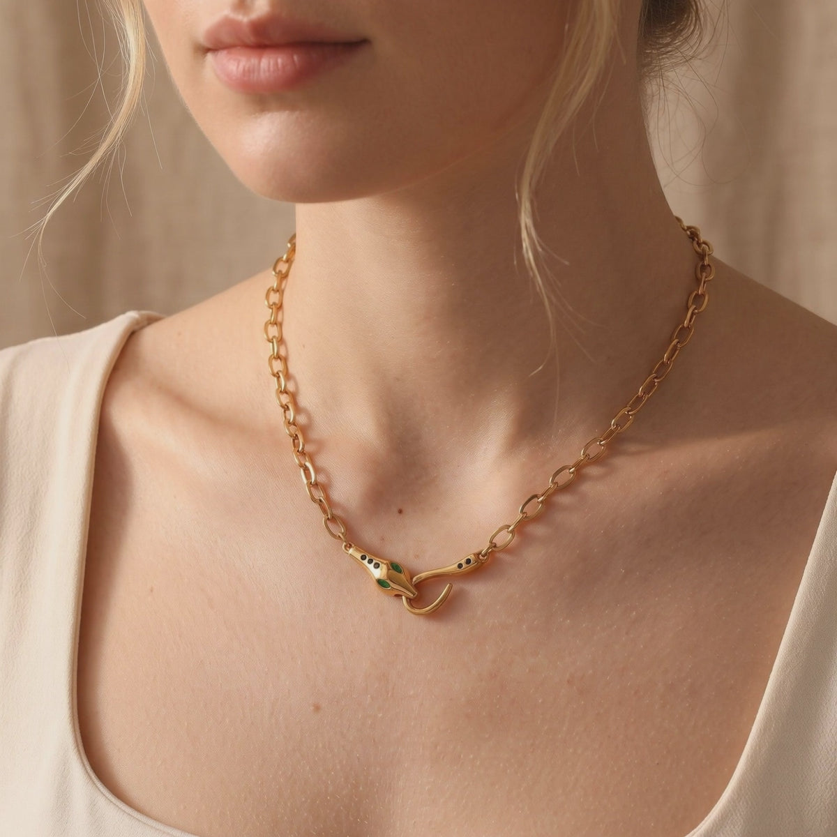 Yellow gold-tone link necklace with a green-eyed snake clasp worn around a model’s neck over a cream top.
