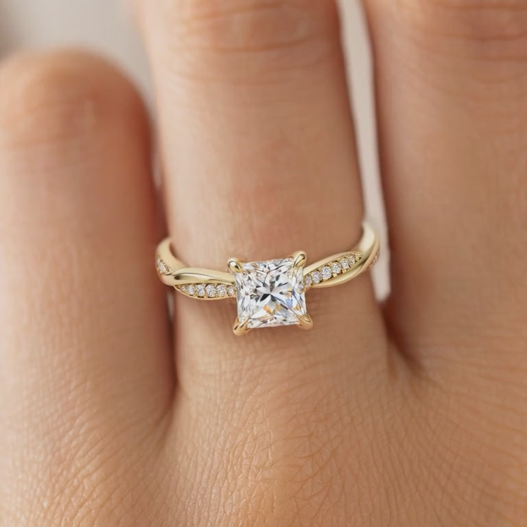 Close-up video of a yellow gold princess-cut moissanite twisted ring worn on a finger.
