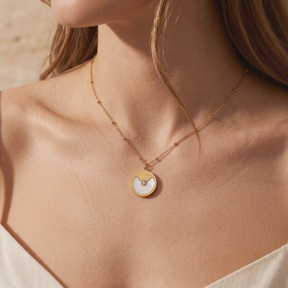 Model wearing the L'Amour gold-tone pendant necklace with a mother-of-pearl inlay and clear central gem.