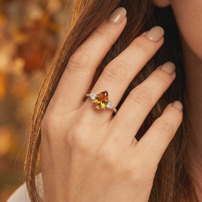 Pear-cut honey simulated topaz ring with clear side stones shown on a hand in solid gold.