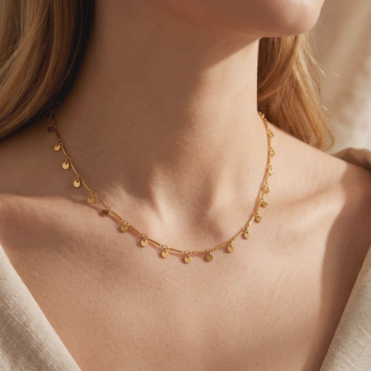 Model wearing a gold-tone bar chain necklace with small disc charms around the collarbone.