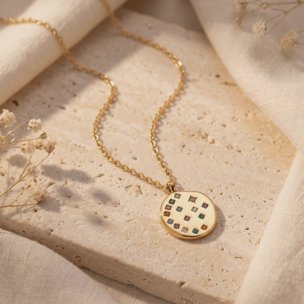 Gold-toned necklace arranged on a textured stone slab, with its round multicolored pendant in the foreground.