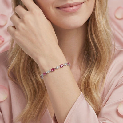 Solid white gold bracelet with oval simulated pink tourmaline stones and round clear accents on a wrist.