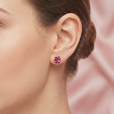Close-up side view of one oval pink tourmaline stud earring in solid yellow gold worn on an earlobe.