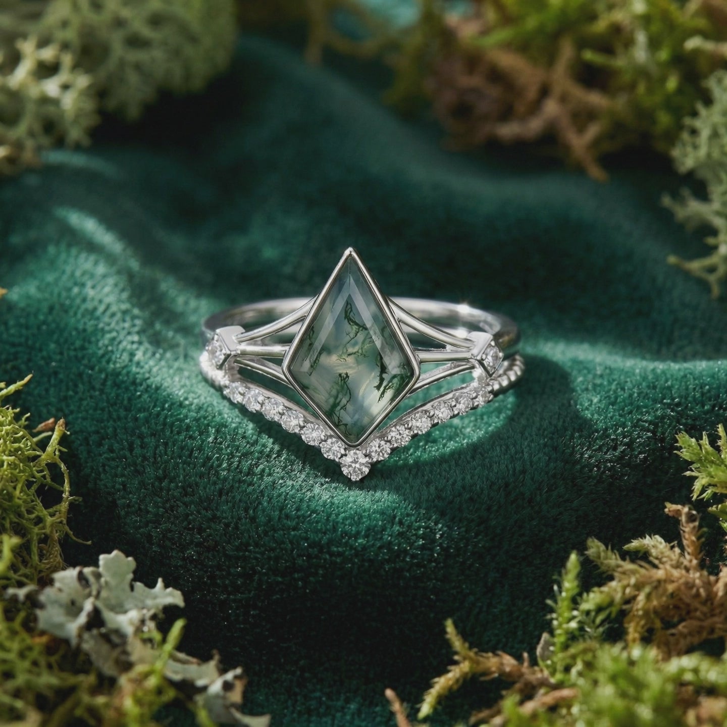 Close-up of a natural moss agate and moissanite solitaire ring with a V-shaped pave chevron band in solid white gold on green velvet.