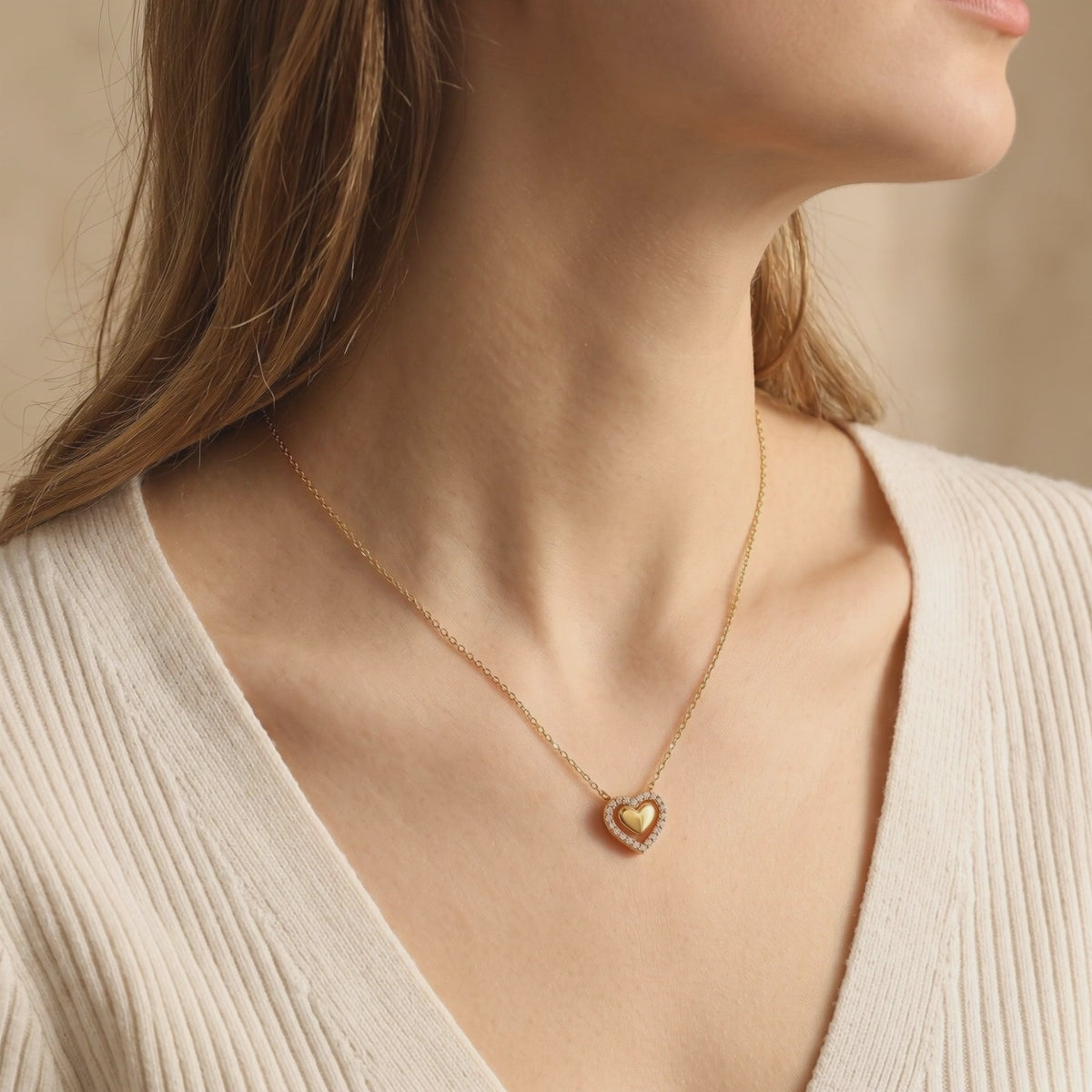 Gold Priscilla double-heart pendant necklace with cubic zirconia, worn with a cream ribbed top.