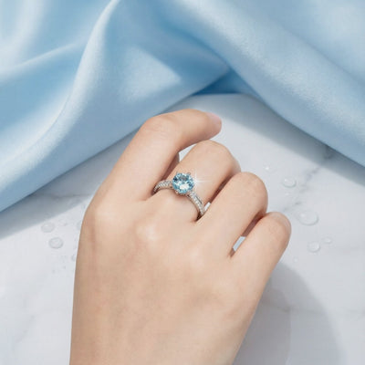 Round simulated aquamarine solitaire ring in solid gold worn on a hand.