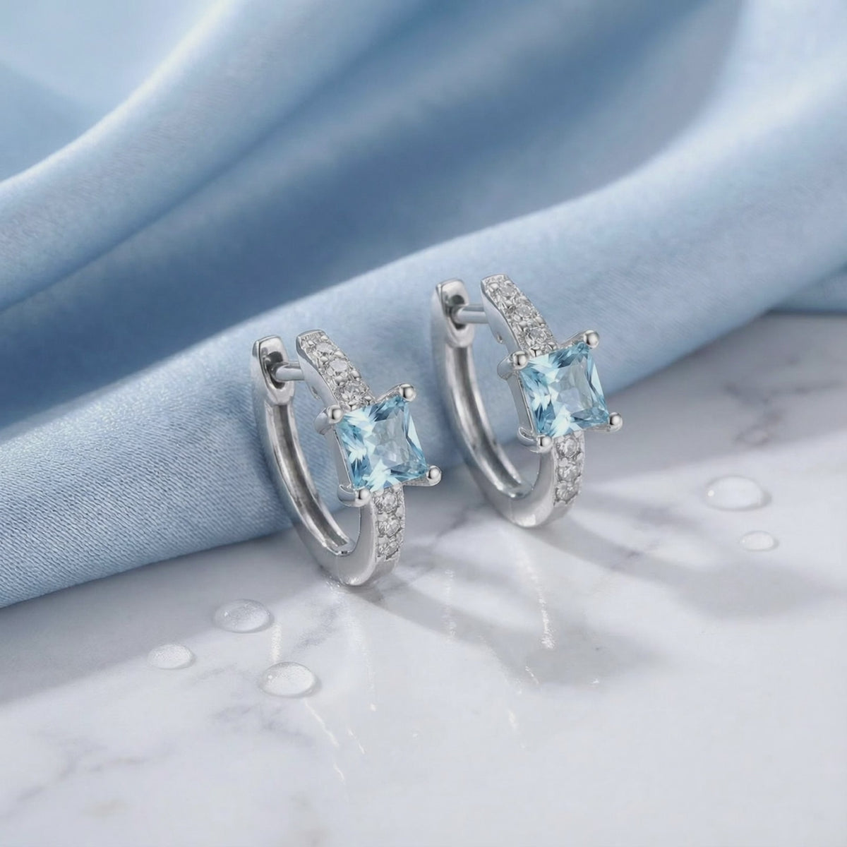 Aira huggie earrings in solid gold with simulated aquamarine stones.
