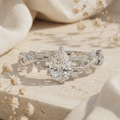 Macro view of pear-cut moissanite ring featuring a detailed solid gold leaf vine band.