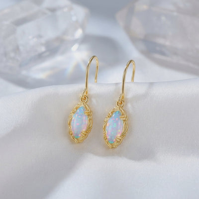 Pair of solid gold drop earrings with mariquesa-cut iridescent opals displayed on white satin.