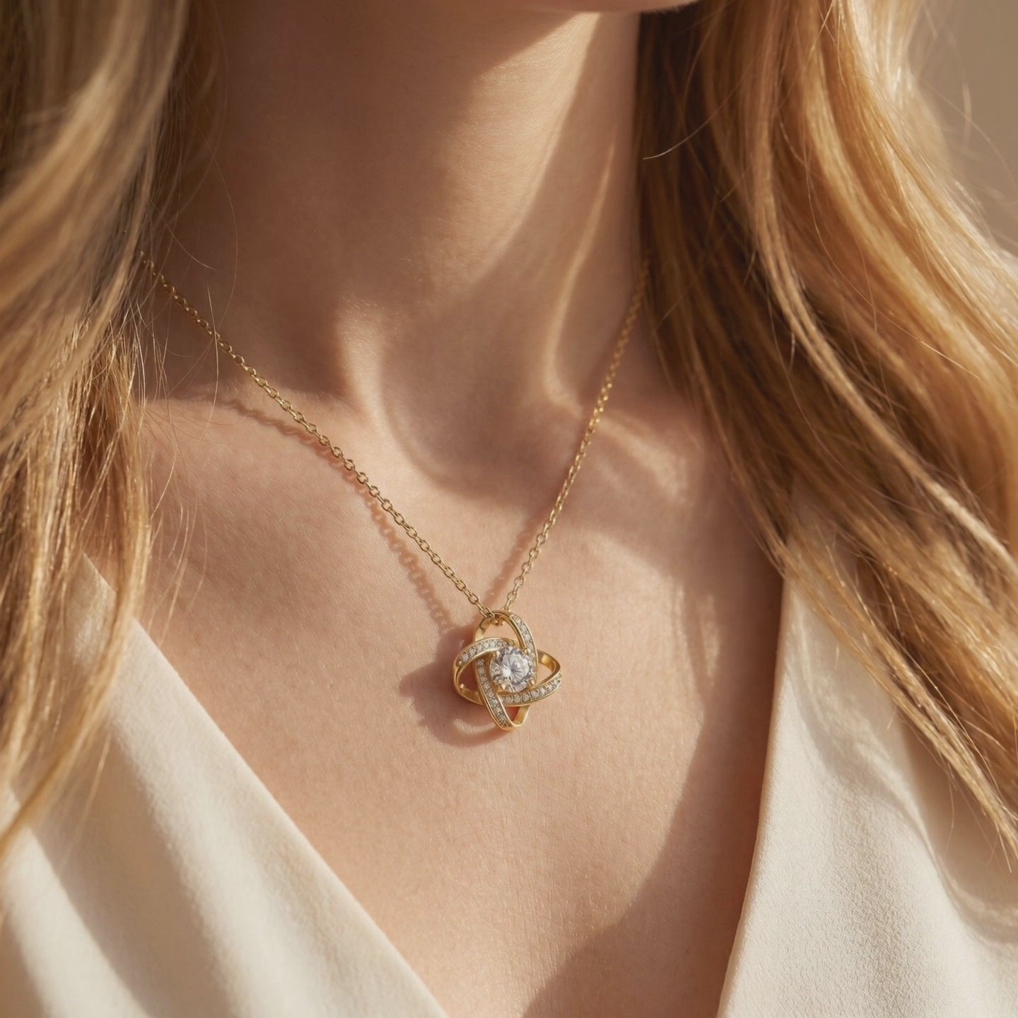 Gold interlocking knot necklace with a clear center stone, shown in a close-up while worn on a person's neck.