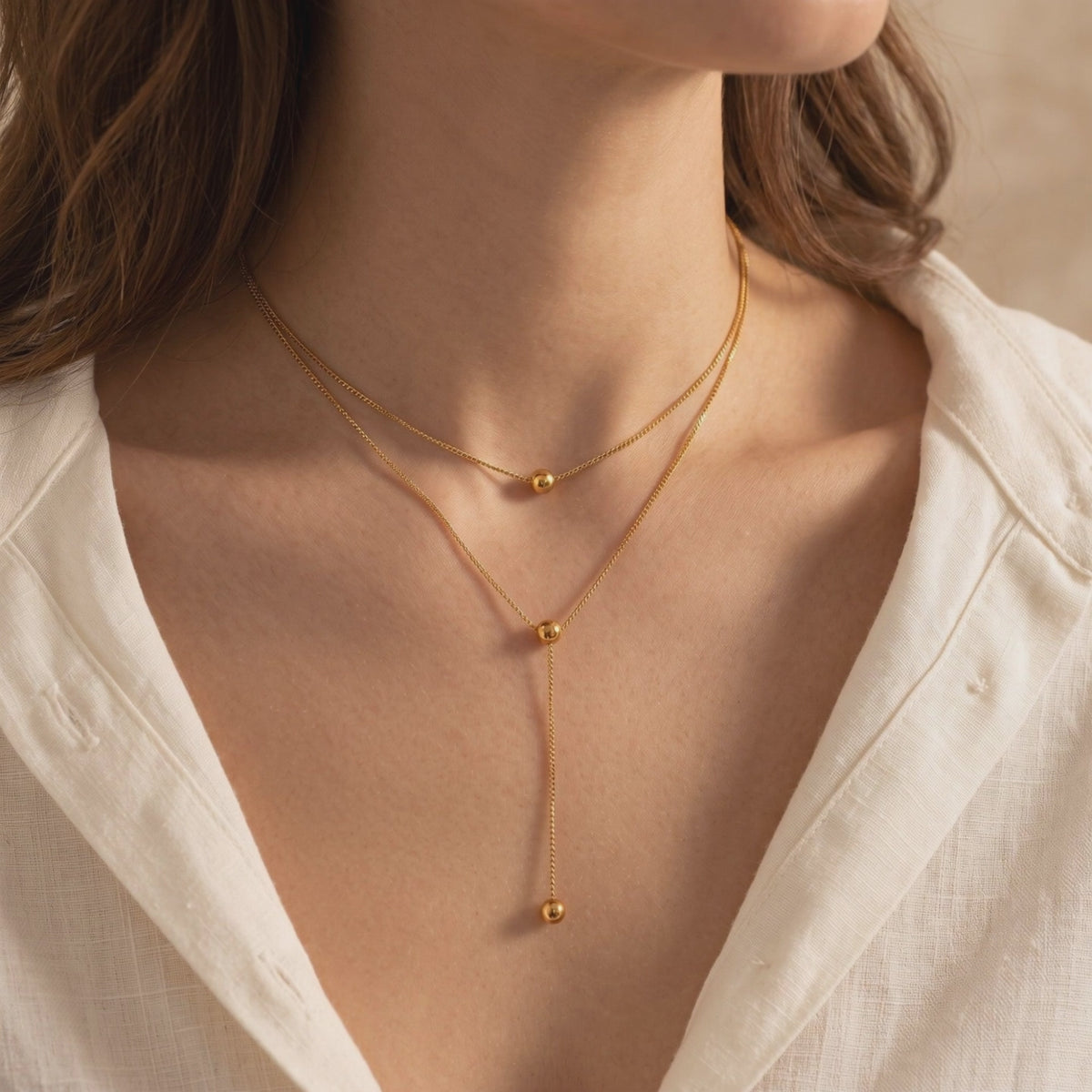 On-model view of a gold-toned double-layered lariat necklace with polished sphere accents.