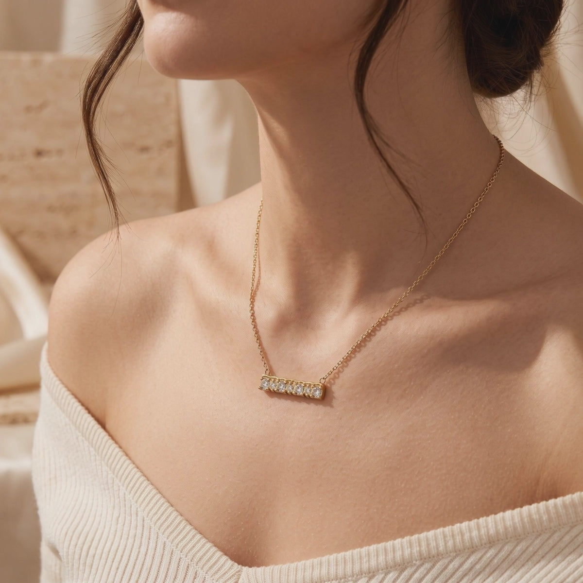 Model wearing a gold-toned horizontal bar necklace with seven clear stones on a cream ribbed top.