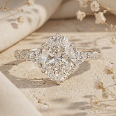 Studio view of an oval moissanite ring with side stones and a twisted solid gold band.