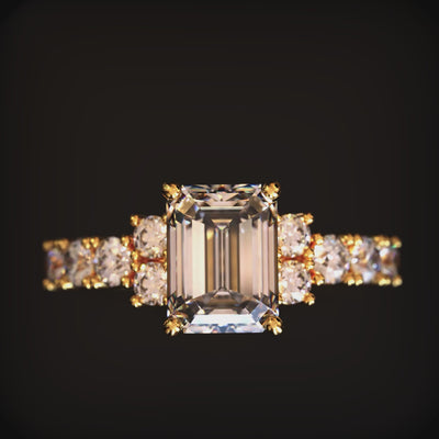 A solid gold ring with an emerald-cut moissanite center stone and pavé side stones.