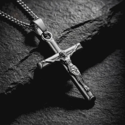 Close-up of a silver crucifix pendant and chain resting on a dark textured stone surface.
