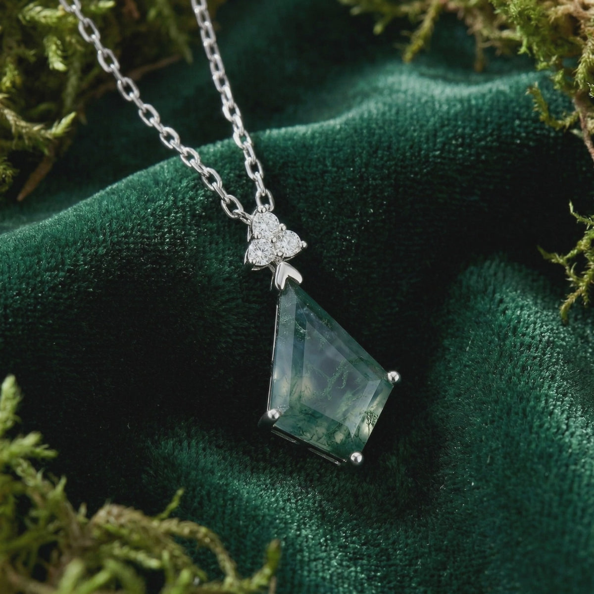 Close-up of a trillion-cut natural moss agate pendant necklace in solid white gold with three clear accent stones on dark green velvet.