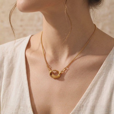 Model wearing a gold-tone braided knot necklace with a white V-neck top.